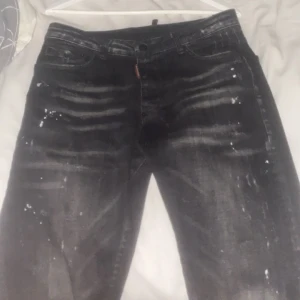 Svarta jeans från Dsquared2 - Snygga svarta jeans från Dsquared2 med coolt slitna detaljer och vita färgstänk. Klassisk femficksmodell med Dsquared2-logga på röd etikett och läderpatch bak. Jeansen har en rak passform och är tillverkade i robust denim.