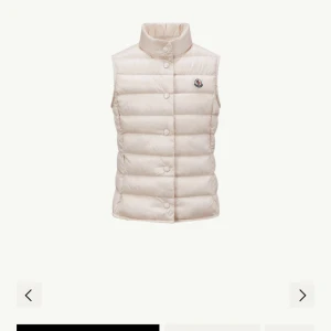 Ljusbeige dunväst från Moncler - Snygg ljusbeige dunväst från Moncler med klassisk quiltad design och hög krage. Västen har tryckknappar framtill och Monclers ikoniska logga på bröstet. Perfekt för lager-på-lager och ger en clean look till din outfit.