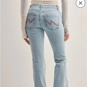 Ljusblå bootcut jeans med slitningar - Säljer ett par lågmidjade ljusblå bootcut jeans med slitna hål på knäna och broderad zigzag-detalj i rosa på bakfickorna.  Använda en gång men var inte min stil så säljer nu dem. Ihop om att dem får en ny ägare 