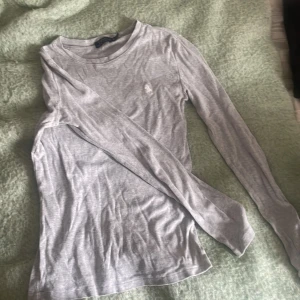 Grå långärmad tröja Polo Ralph Lauren - Säljer en stilren grå långärmad tröja från Polo Ralph Lauren i mjuk bomull. Tröjan har rund halsringning och den klassiska broderade loggan på bröstet. Perfekt för en clean och enkel look.