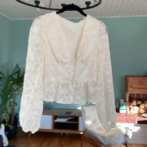 Vit spetsblus med knappar och volang - Skit snygg vit blus i spets med v-ringning i stolek 152. Långa ärmar med lätt puff och struktur i tyget. Skriv för mer info