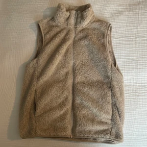 Beige fluffig fleeceväst med dragkedja (UNIQLO) - Mysig beige väst i fluffig fleece med hög krage och hel dragkedja framtill. 