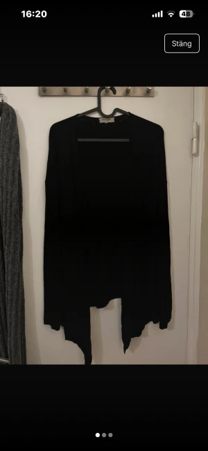 Svart kofta från Basicyou - Svart, tunn och flowy kofta från Basicyou (Ullared) med långärmad design och öppen framtill. Materialet är mjukt och lätt, perfekt för lager-på-lager. Koftan har en asymmetrisk nederkant som ger en chill och avslappnad vibe.