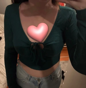 Mörkgrön croppad ribbad topp - Säljer en mörkgrön croppad topp med ribbad struktur och lång ärm. Toppen har en djup v-ringning och snygg snörning framtill som ger en cool detalj. Perfekt att styla med höga jeans för en trendig look.