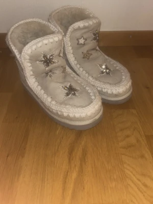 Beige boots från Mou med broderade stjärnor - Säljer ett par beige boots från Mou med broderade och glittriga stjärnor. Skorna har en rund tå, platt sula och är fodrade med mjukt pälsmaterial. Dekorativa stickade detaljer runt kanten ger en mysig vinterkänsla. Nästan oanvända.