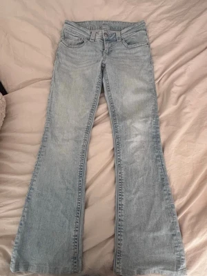 Bootcut ljusblå jeans - Snygga ljusblå bootcut jeans  med klassisk femficksdesign och knappstängning. Jeansen har en lätt tvättad look och är tillverkade i mjukt denimtyg som sitter skönt. Perfekt för dig som gillar retrovibbar och vill ha en cool siluett.