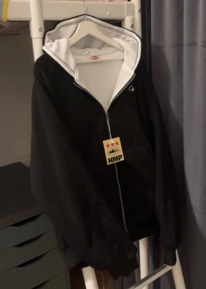 svart Corteiz HMP thermal zip hoodie  - Svart hoodie från HMP i storlek Large med vit meshfoder i huvan och snyggt broderad logga på bröstet. Tröjan har hel dragkedja framtill och en stor huva som ger en chill vibe. Perfekt för dig som gillar streetwear och vill ha något bekvämt och stilrent.