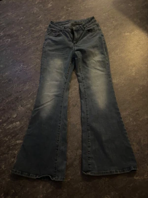 Blå bootcut jeans med slitningar - Snygga blå jeans med bootcut passform och lätt slitna detaljer på låren. Klassisk femficksmodell med knapp och dragkedja framtill. Jeansen har en mörkblå ton med ljusare partier och är tillverkade i jeansmaterial.