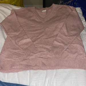 Rosa stickad tröja från Vila - Mysig rosa stickad tröja från Vila i storlek M. Tröjan har v-ringning, långa ärmar och breda ribbade muddar vid ärmslut och nederkant. Perfekt för lager-på-lager och chill dagar.
