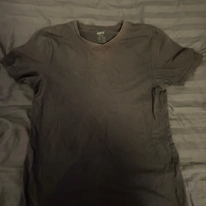 Mörkgrå t-shirt från Pepperts - En enkel och stilren mörkgrå t-shirt från Pepperts i storlek 158/164. T-shirten har rund hals och korta ärmar, tillverkad i mjuk bomull som är skön mot huden. Perfekt för dig som gillar basic och avslappnad stil.