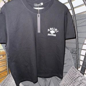 Svart Amiri Records t-shirt - Svart t-shirt från Amiri med tryck 'AMIRI RECORDS' fram och bak. Klassisk rund hals och korta ärmar. Materialet är mjuk bomull och passformen är normal. Snygg streetwear-vibe med coolt print som sticker ut.