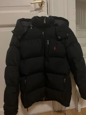 Polo Ralph Lauren vinterjacka - Säljer en jättesnygg och varm vinterjacka från Polo Ralph Lauren med avtagbar luva. Jackan är köpt på Plick och säljer nu vidare den. Jackan har tagits väl hand om, kontakta mig för mer information/bilder! Ordinarie pris är runt 6000kr