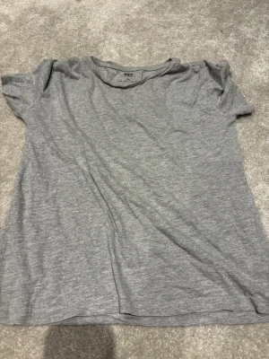 Grå t-shirt från 157 i XS - En enkel och mjuk grå t-shirt från 157 i storlek XS. T-shirten har rund hals och korta ärmar, tillverkad i 90% bomull och 10% viskos för en skön känsla. Perfekt för dig som gillar basic och stilrena plagg.