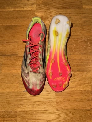 Adidas F50 Elite fotbollsskor stl 41 1/3 - Säljer ett par Adidas F50 Elite fotbollsskor i storlek 41 1/3 med cool design i rött, vitt och inslag av gult. Ovandelen är i syntetmaterial med svart detalj längs sidan och spetsig tå för extra speed. En minimal slitage-skada vid höger tå, men annars är de i bra skick. Priset är aningen förhandlingsbart 