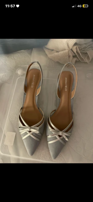 Silverfärgade pumps från Anna Field - Helt oanvända, ny utan prislapp. Snygga pumps i silver från Anna Field med spetsig tå och låg klack. Skorna har en öppen häl och dekorativa band med rosett framtill.