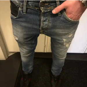 Jack & Jones Slim Fit Jeans, W29 L32 – tvättad blå med slitna detaljer 👖 - Jack & Jones Slim Fit Jeans, W29 L32 – tvättad blå med slitna detaljer 👖  Stilren och modern slim fit-jeans från Jack & Jones i snygg, tvättad blå nyans. Jeansens smala passform sitter tajt längs benen och framhäver siluetten – perfekt för dig som uppskattar streetstyle med edge. Den svarta skinnliknande fickan framtill ger en unik, lite rå detalj som sticker ut. 	•	Storlek: W29 / L32 	•	Design: Klassisk femficksmodell & knappgylf 	•	Passform: Slim/skinny – sitter tight längs benen 	•	Färg & fin