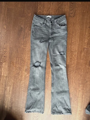 Grå bootcut jeans från Gina Tricot stl.152 - Snygga grå jeans från Gina Tricot i bootcut-modell. Jeansen har slitna detaljer på benen och klassisk femficksdesign. Tillverkade i stretchig denim för skön passform. Perfekta för dig som gillar en trendig och avslappnad look.