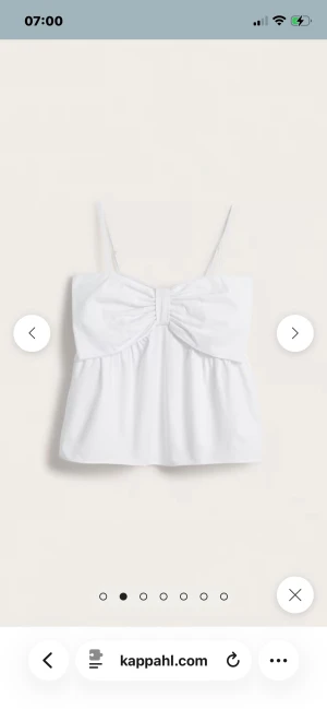 Vit linnetopp med rosett från Kappahl - Supersöt vit linnetopp från Kappahl med tunna axelband och en stor rosettdetalj framtill. Toppen har en luftig passform och är tillverkad i mjuk bomull, perfekt för varma dagar. Enkel att styla med jeans eller kjol för en fräsch look.