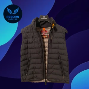 Parajumper Dunväst svart - Snygg svart dunväst från Parajumpers med quiltad design och hög krage. Västen har dragkedja framtill, två fickor med dragkedja och ikonisk logga på ryggen. Perfekt för lager-på-lager och streetstyle. Lätt och smidig att bära.