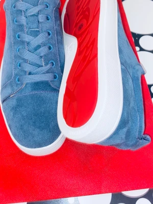 Blå mocka sneakers från Louboutin - Snygga blå sneakers från Christian Louboutin i mjuk mocka med klassisk röd sula och vita kanter. Skorna har rund tå, snörning och blå detaljer på öglorna. Perfekt för dig som vill sticka ut med exklusiv stil och ikonisk design.
