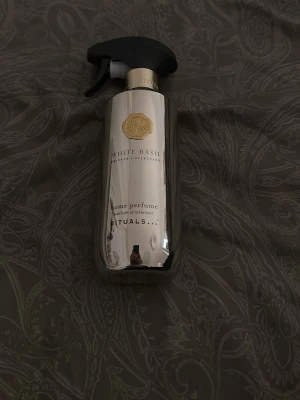 Rituals White Basil rumsdoftspray - Säljer en stilren rumsdoftspray från Rituals i doften White Basil. Flaskan är silverfärgad med svart spraymunstycke och gulddetaljer. Perfekt för att fräscha upp hemmet med en lyxig och fräsch doft. Enkel att använda och snygg att ha framme.