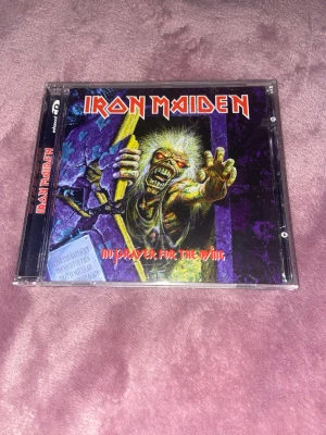 Iron Maiden CD No Prayer For The Dying - Iron Maiden CD-album 'No Prayer For The Dying' i plastfodral med färgstark omslagsbild och låtlista på baksidan. Perfekt för dig som samlar på klassisk heavy metal eller vill ha en ikonisk skiva i din samling.
