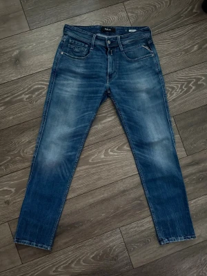 Blå Replay Anbass jeans slim fit - Snygga blå Replay Anbass jeans i slim fit och klassisk femficksdesign. Jeansen har en lätt tvättad look med slitningar på låren och knäna. Tillverkade i mjukt bomullsmaterial med en touch av stretch för extra komfort.