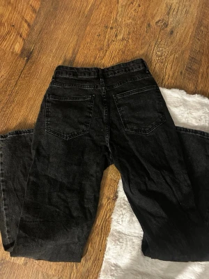 Svarta wide jeans med hög midja - Säljer ett par svarta jeans med hög midja och breda ben. Klassisk femficksmodell med knapp och dragkedja framtill. Jeansen har en avslappnad och trendig passform, perfekta till en cool streetstyle-look.