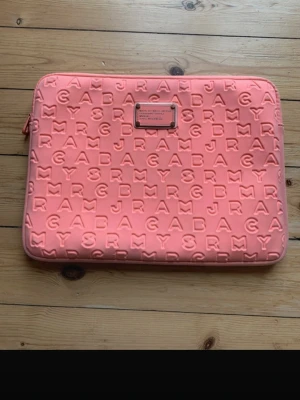 Korall datorfodral från Marc by Marc Jacobs - Säljer en jätte snygg rosa datorväska från Marc by marc Jacobs. Den är använd fåtal gånger och är i jättebra skick dock så  har den en super liten fläck som man knappt ser. Perfekt för att bära din laptop med stil. Skriv ifall ni har fler frågor (finns inte att fylla i korall färg så kommer fylla i rosa)🩷🩷🩷