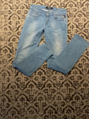 Ljusblå Replay jeans slim fit - Snygga ljusblå jeans från Replay med slim fit och klassisk femficksdesign. Jeansen har en fräsch tvätt och silverfärgade detaljer vid fickorna. Perfekta för dig som gillar en stilren och modern look.