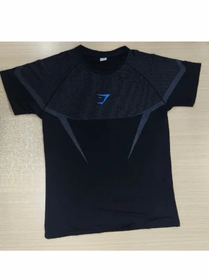 Svart träningstshirt från Gymshark og midnight  - Snygg svart t-shirt från Gymshark med korta ärmar och sportig design. Har gråa detaljer och ett blått Gymshark-logo på bröstet. Materialet är lätt och andas, perfekt för gymmet eller löprundan.