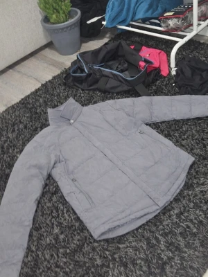 Grå quiltad dunjacka - Snygg grå dunjacka från tesla med quiltad design och hög krage. Jackan har dragkedja framtill och två sidofickor med dragkedja. Perfekt för kyliga dagar och enkel att matcha med olika outfits. 