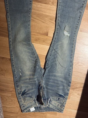 ”Smuts” grå, slitna utsvängda jeans  - Ett par gråa jeans med slitningar och utsvängda ben. Storleken är i längd och bredd. B-26 och L-32 endast provade. 