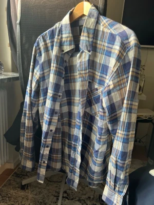 Blåvit rutig skjorta från Blend - Klassisk rutig skjorta från Blend i blått, vitt och beige. Skjortan har lång ärm, knappar framtill och en bröstficka. Tillverkad i mjuk bomull och har en avslappnad passform som passar perfekt till jeans eller chinos.