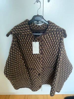 Zara Jacka  - Unik kappa från Zara i brun och beige färg med rutigt mönster. Kappan är tillverkad i ull och har en loose passform med stora knappar framtill och bred krage. Perfekt för dig som vill sticka ut med en retrovibe.