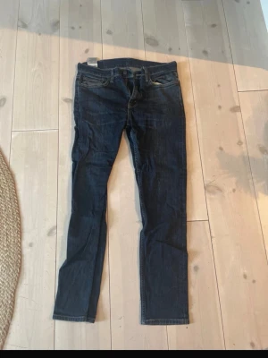 Levi's mörkblå jeans - Säljer ett par klassiska Levi's jeans i mörkblå tvätt. Jeansen har normal passform med raka ben och fem fickor. Tillverkade i slitstark bomullsdenim med snygga kontrastsömmar och den ikoniska Levi's-lappen bak i midjan.