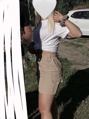 Beige kortkjol med fickor - Säljer en beige kortkjol med stora sidofickor och hög midja. Kjolen har en enkel design med knapp och dragkedja framtill, samt bälteshällor. Perfekt för en avslappnad och trendig look.