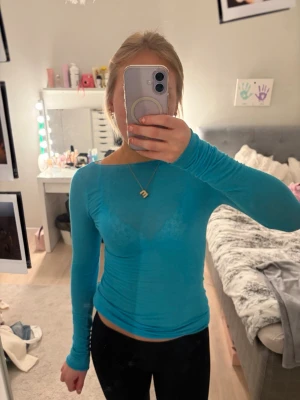 Turkos långärmad topp i mesh - Säljer en turkos långärmad topp i meshmaterial. Toppen är tight och har en rund halsringning. Perfekt att styla med jeans eller kjol för en trendig look.