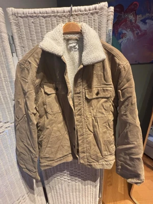 Beige teddyjacka i manchester från H&M - Säljer en beige teddyjacka från H&M i manchester med vit fluffig teddykrage och foder. Jackan har två bröstfickor med knappar och två sidofickor. Perfekt för höst och vinter, riktigt mysig och trendig oversized look.
