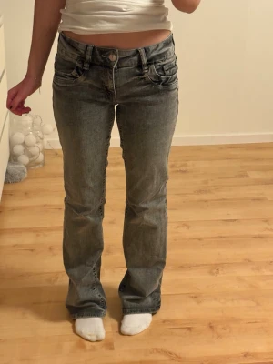 Grå bootcut jeans med låg midja - Säljer ett par grå bootcut jeans med låg midja. Jeansen har klassisk femficksdesign, knappgylf och är tillverkade i mjukt denimtyg. Passformen är normal och benen har en lätt utsvängd siluett. Perfekta för en avslappnad och trendig look.