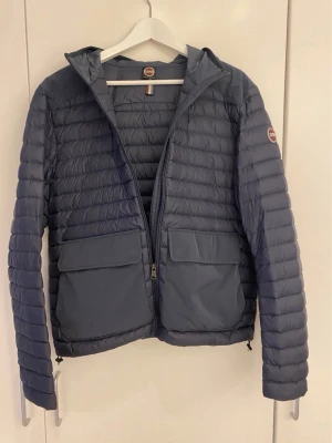 Colmar jacka - Snygg blå dunjacka från Colmar med huva och två stora fickor framtill. Jackan har quiltad design, dragkedja och Colmar-logga på ärmen. Perfekt för kyliga dagar och enkel att matcha med olika outfits.