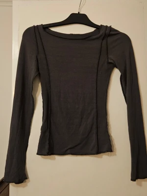 Mörkgrå långärmad topp - Säljer en mörkgrå långärmad topp med figurnära passform. Toppen är tillverkad i ett tunt, stretchigt material och har synliga sömmar som ger en trendig look. 