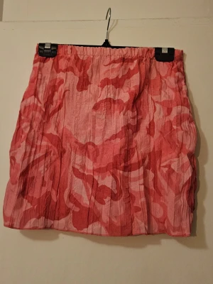 Rosa mönstrad kortkjol från NA-KD - Snygg kortkjol från NA-KD i olika rosa nyanser med abstrakt mönster. Kjolen har resår i midjan och är tillverkad i ett lätt, skrynkligt tyg som ger en cool och avslappnad look.