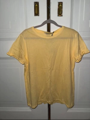 Gul basic t-shirt från NA-KD - En enkel och fräsch gul t-shirt från NA-KD i mjuk bomull. T-shirten har rund halsringning och korta ärmar, perfekt för en avslappnad och stilren look. Passformen är normal och färgen är ljusgul, vilket gör den lätt att matcha med allt.