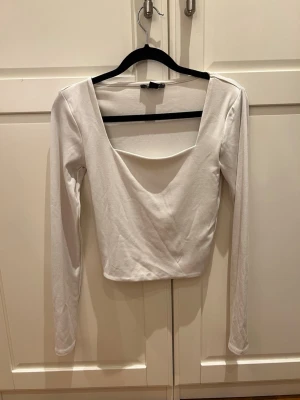 Vit långärmad croppad topp - Säljer en vit långärmad topp med djup, bred urringning och croppad passform. Toppen har en enkel och stilren design som passar perfekt till jeans eller kjol. 