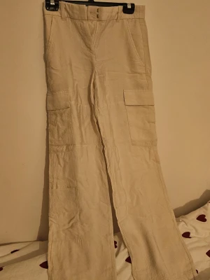 Beiga cargopants i linne - Snygga beiga cargopants med raka ben och stora fickor på sidorna. Tillverkade i ett luftigt linnematerial som passar perfekt för en avslappnad och trendig stil. 