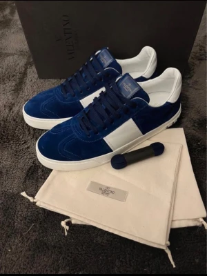 INTRESSEKOLL!DISKUTERBART PRIS! - Snygga Valentino Rockrunner sneakers i mörkblå mocka med vita detaljer och platt sula. Skorna har rund tå, klassisk snörning och en kontrasterande vit panel på sidan. Perfekta för dig som vill ha en exklusiv och trendig look. BOX INGÅR! ALLA NITAR ÄR KVAR,KOM MED PRIS😶‍🌫️