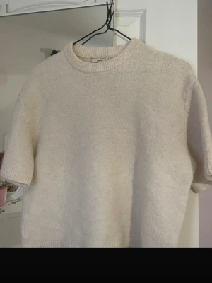 Beige stickad topp - Superfin beige stickad topp från Gina Tricot med korta ärmar och rund halsringning. Mjuk och skön, perfekt till jeans eller kostymbyxor. Enkel och stilren design som passar till många olika looks.
