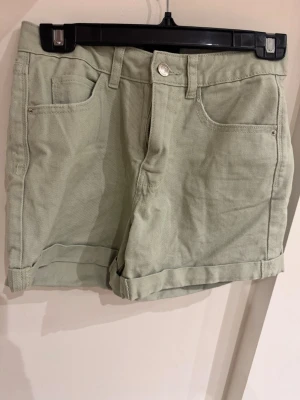 Ljusgröna denimshorts Vero Moda XS - Snygga ljusgröna denimshorts från Vero Moda i storlek XS. Klassisk femficksmodell med uppvikta benslut och bälteshällor. Perfekta för varma dagar och enkla att matcha med allt. Tillverkade i bomull för en skön känsla.