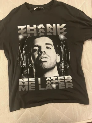 Drake t-shirt -thank me later - Denna svarta t-shirt hyllar Drakes debutalbum Thank Me Later med ett stilrent grafiskt tryck i gråskala av artistens ansikte. Ovanför motivet syns en glittrande signaturdetalj och metalliskt skimrande texten “THANK ME LATER” som ger tröjan en exklusiv känsla. Perfekt för fans av Drake eller samlare av musikmerchandise som vill bära en ikonisk del av hiphophistorien.